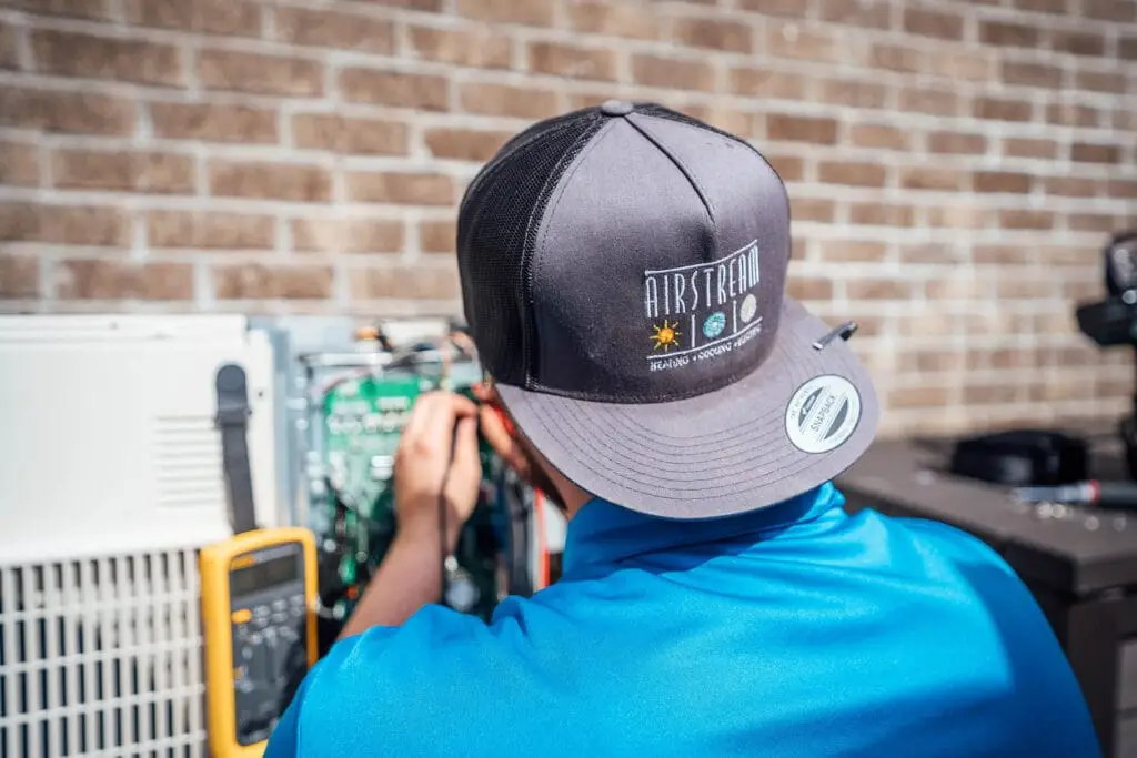 Airstream Services technician working on wiring during an AC unit installation, wearing a branded company cap.