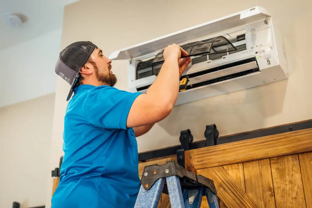 A gentlemen from Airstream Services wearing a blue collared shirt, standing on a ladder. He is repairing a ductless mini system (ac repair) that is on a wall.