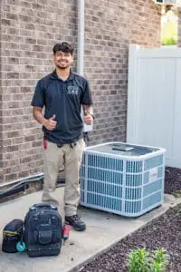Smiling Airstream HVAC technician giving a thumbs-up next to a new outdoor air conditioning unit and tool bag.