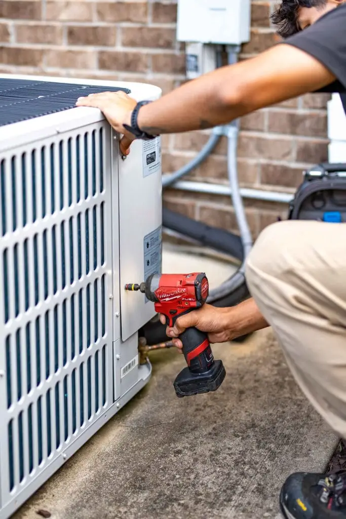 Airstream HVAC technician using a red power drill to work on the side panel of an outdoor air conditioning unit.