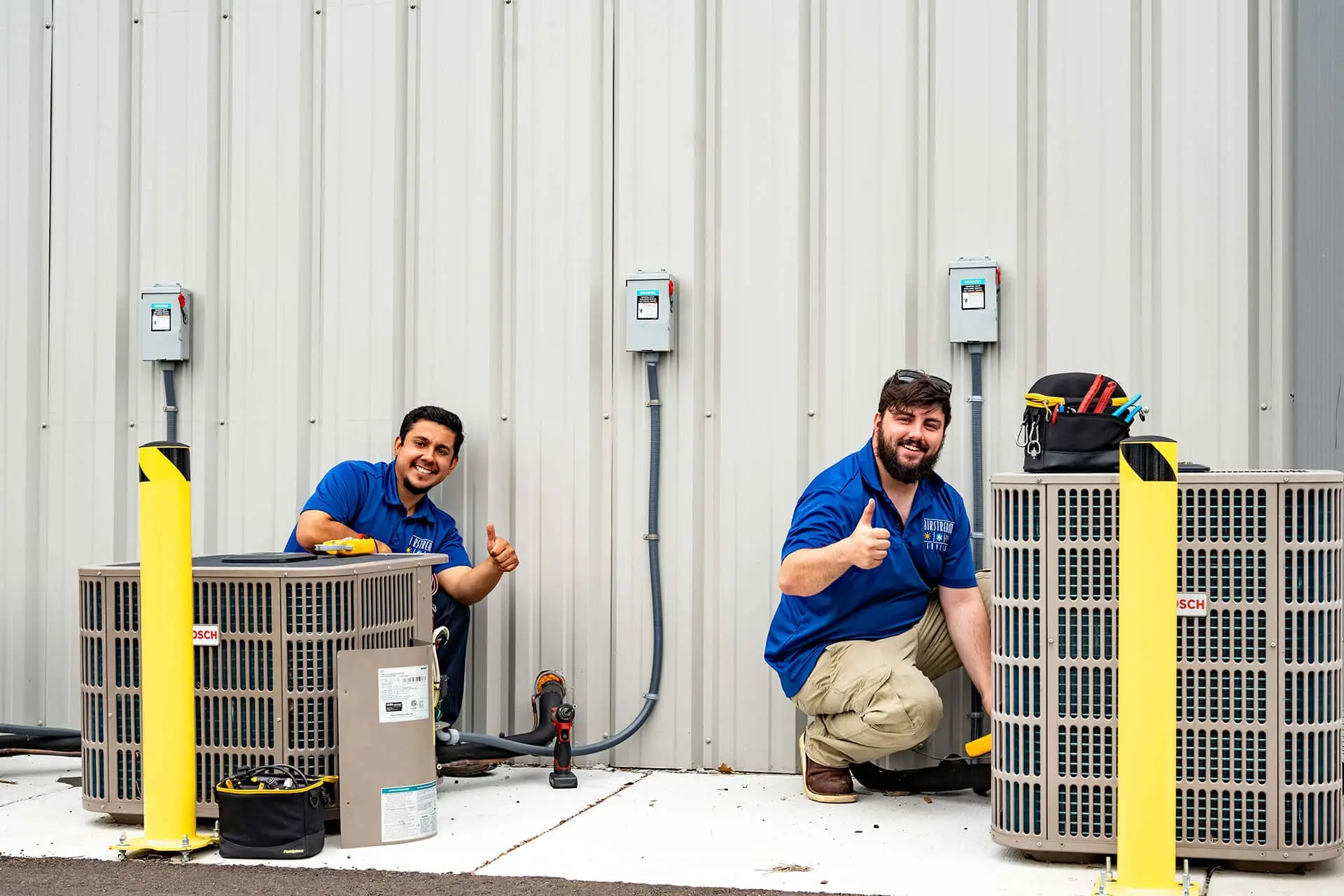Airstream Services HVAC technicians giving a thumbs-up while installing new outdoor air conditioning units at a commercial property in Middle Tennessee.