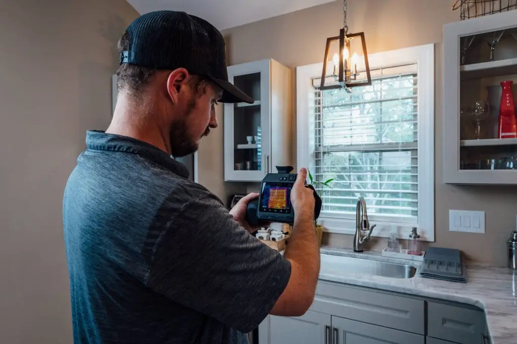 Airstream Services technician performing a thermographic inspection in a residential kitchen using a thermal imaging camera.
