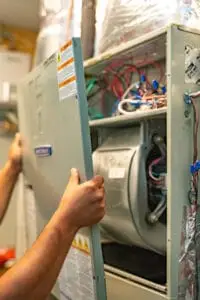 Technician opening an HVAC unit panel to inspect wiring and electrical components, a common source of electrical burning smells in homes.