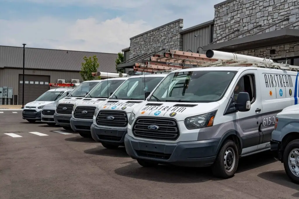 A line of branded Airstream Plumbing, Heating & Air service vans parked outside a building.