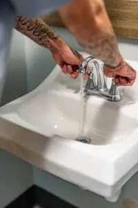 Person checking water flow from a bathroom sink faucet to diagnose low water pressure.