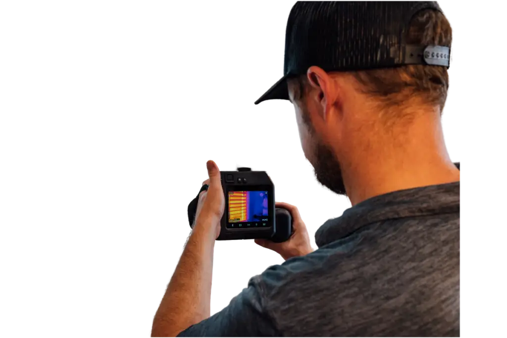 Technician from behind, wearing a cap and holding a thermal imaging camera with a colorful display.