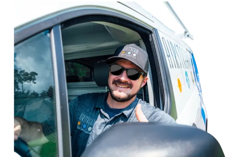 Smiling Airstream Plumbing, Heating & Air technician in sunglasses giving a thumbs-up from inside a service van.