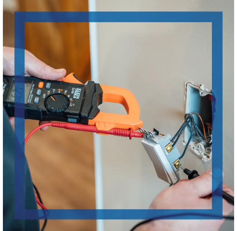 Electrician using a clamp meter and probes to test an electrical outlet or switch during diagnosis.