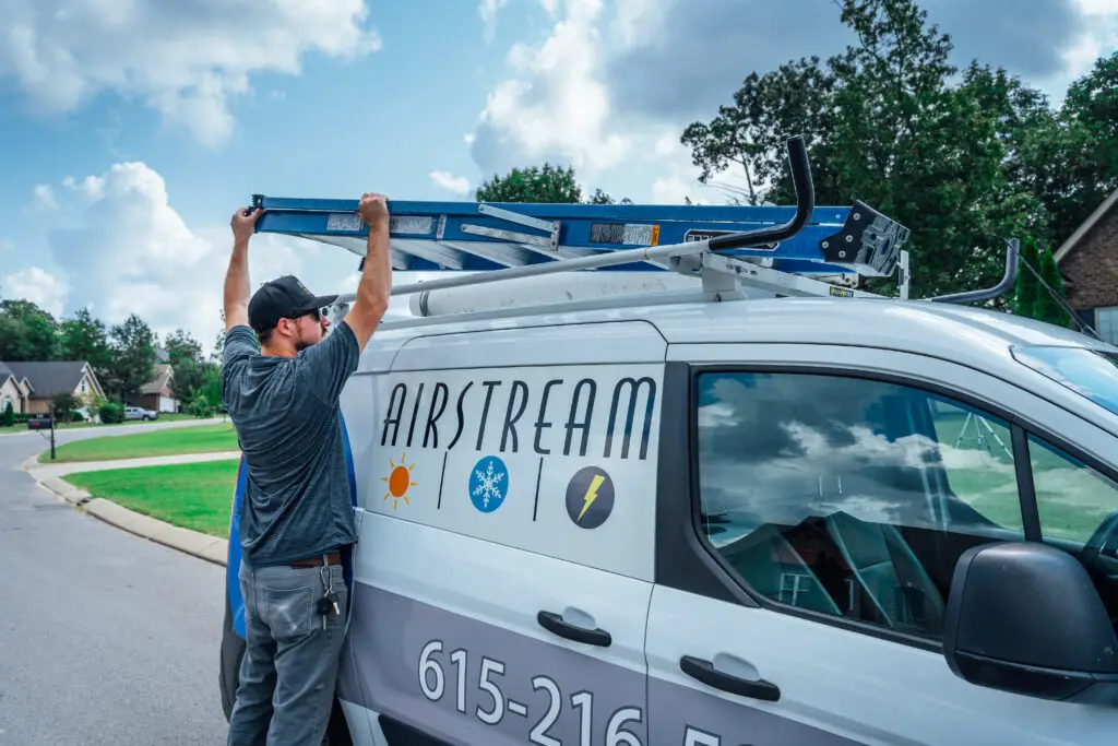 Airstream technician securing a blue ladder to the roof rack of a branded service van.